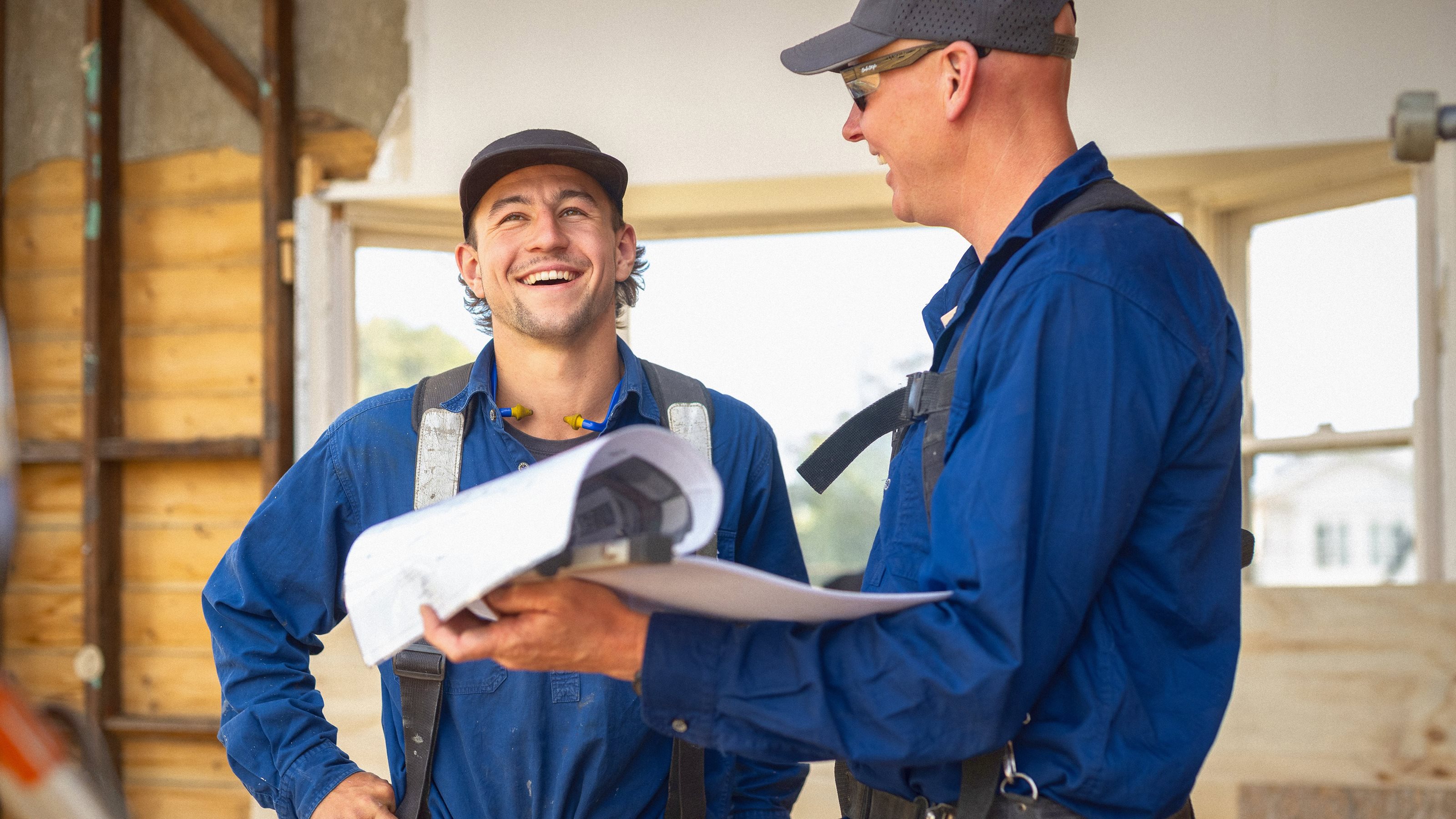 Image of two workers looking at site plans. They are engaged in joyful conversation.