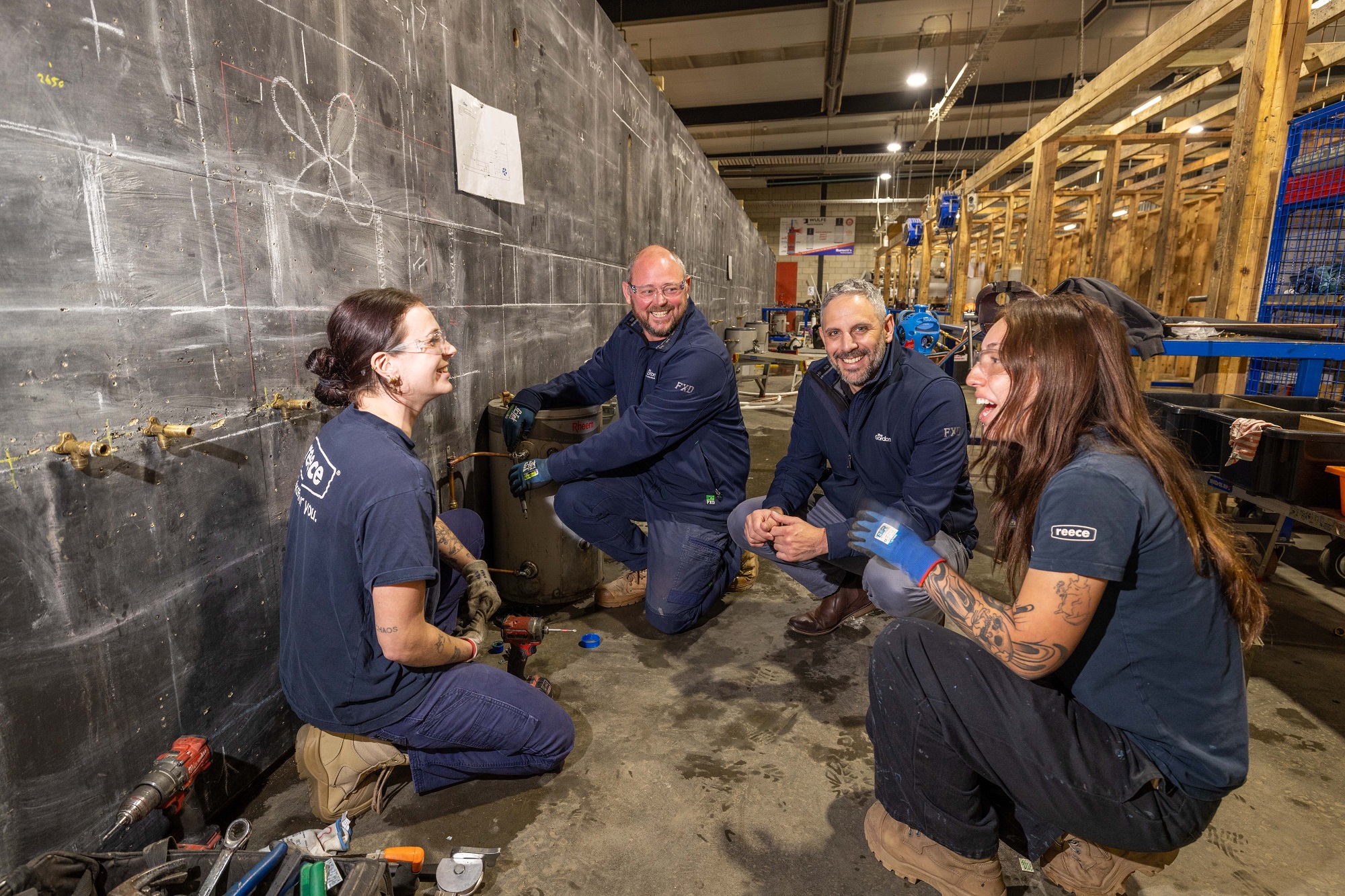 Article subject Andy kneeling on the floor with a small a group of other tradies in a work training environment.