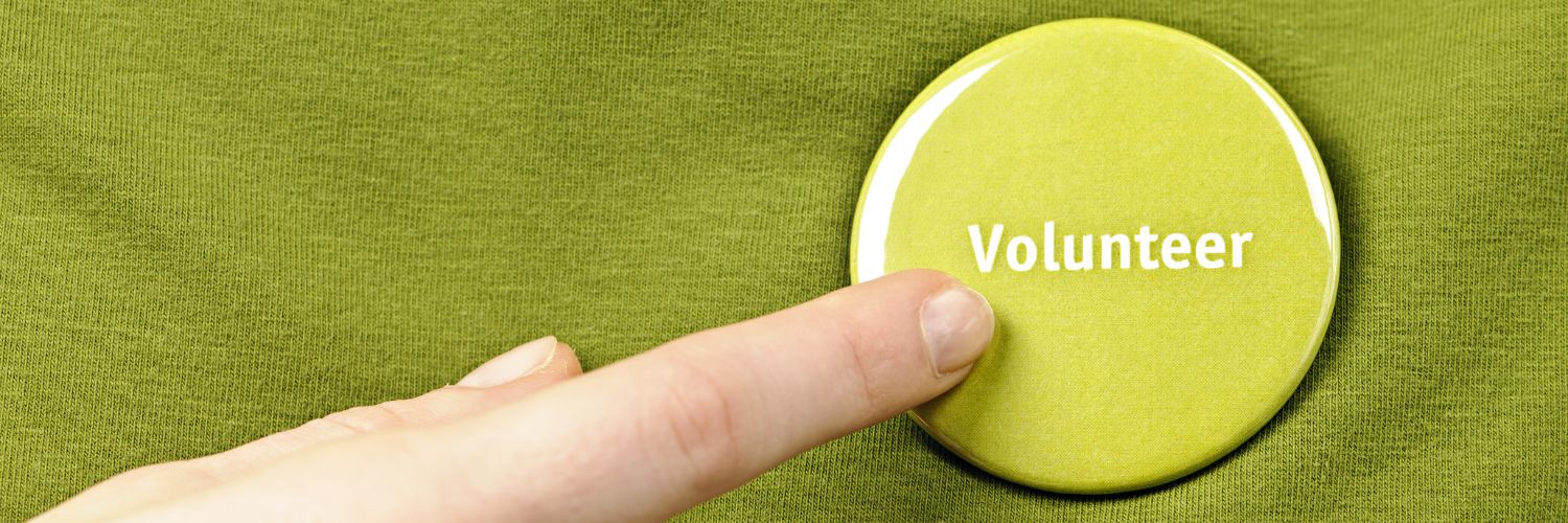Finger pointing to a green button with the word “Volunteer” on a green background.